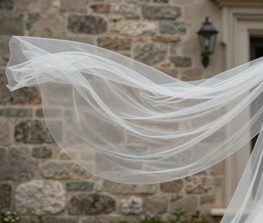 A close-up shot of a bride's sheer white veil floating in the breeze. In the background, a North American / European stone villa wall in muted taupe provides a textured, elegant backdrop.