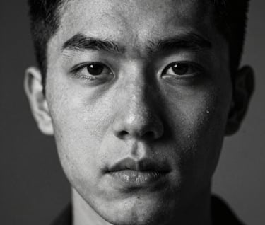 A sharp, high-contrast artistic portrait in black and white. The lighting creates deep shadows, emphasizing the subject's expression. International / Professional.