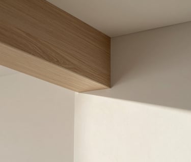 Close-up detail of architectural materials: a textured #8D6B5F timber beam meeting a smooth #F9F6EE wall, with a sharp shadow cast by strong afternoon sunlight. Minimalist and professional composition.