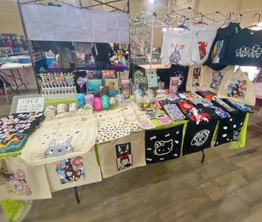 Un puesto de venta de productos de anime con bolsos, playeras,  pines en un bazar
