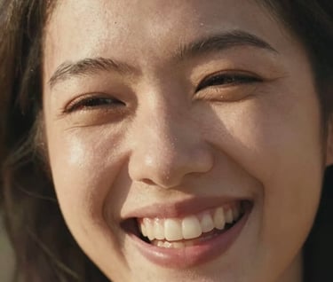 A deeply personal and cinematic close-up of a woman's joyful, authentic smile. North American / US setting. The lighting is warm and sun-drenched, emphasizing genuine human emotion and a friendly, inviting mood.