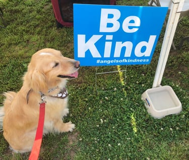 A Therapy Dog sitting next to a "Be Kind" sign