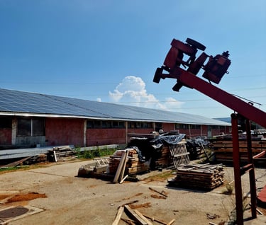 production site with solar panels on the roof and a pile of wood in the yard