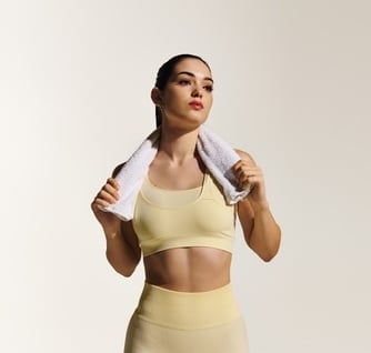 Woman in yellow fitness apparel with a white towel around her neck.