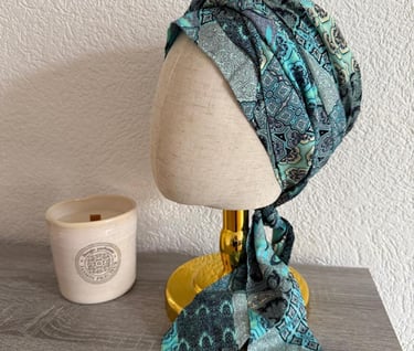 Turban en tissu vert et bleu à motifs, présenté sur un présentoir de tête.