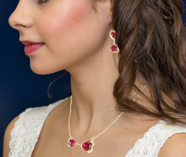 a woman wearing a gold eternal love knot necklace and earrings with a ruby heart