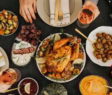 A holiday food spread with turkey, cheese, grapes, mushrooms, brussel sprouts, squash, cranberry sauce and wine