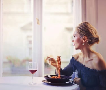 A woman enjoying a bowl of spaghetti in tomato sauce and glass of red wine