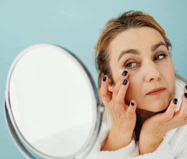 A woman applying eye cream in front of a mirror
