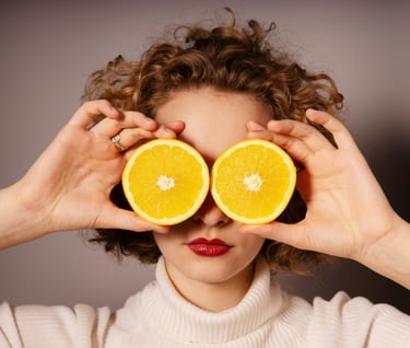Woman holding up 2 orange slices to her face to cover her eyes.