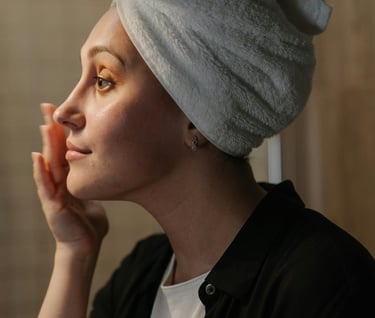 A woman in a black shirt and toweled hair applying a skincare product