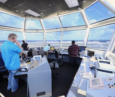 a man in a blue shirt is standing in front of a large window in an airport control tower