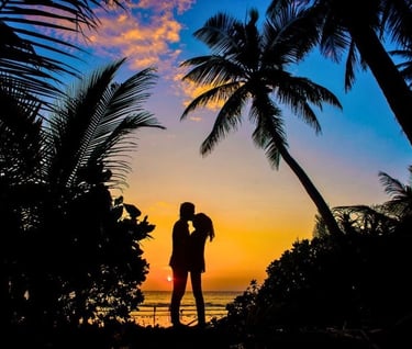a couple kissing in front of a sunset on a tropical island