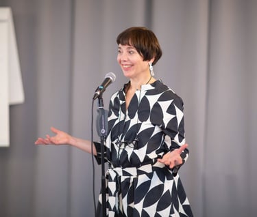 Female public speaking trainer, smiling behind microphone with confident body language. 