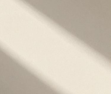 Large, grainy, underexposed photo of a morning shadow falling across a textured wall. The light is soft and hazy. Editorial zine style, very minimal, emphasizing whitespace and the brand's cream palette (#F8F3EC).