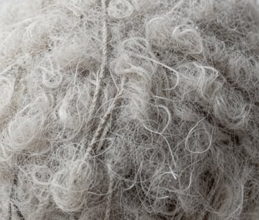 Macro photography of raw organic wool texture. Soft focus on the edges, light gray and white tones. Clean, elegant, and professional aesthetic typical of Northern European design.