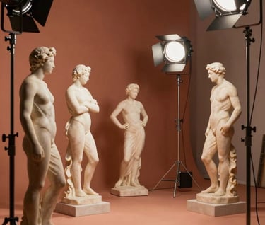 Wide shot of an artistic film set, showing a mix of classic marble sculptures and modern lighting equipment. The scene is bathed in a warm terracotta (#A3533F) glow, blending the professional commercial world with artistic sensibility.