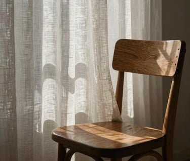 A poetic and artistic close-up of light filtering through a sheer, textured linen curtain, casting delicate and abstract geometric shadows onto a beautifully designed wooden chair. The image feels deeply quiet, high-fashion, and sophisticated.
