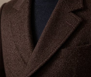 Close-up detail shot of a handsomely tailored coat collar in dark espresso brown wool, showcasing exquisite handmade stitching. Professional editorial photography, soft side lighting, rich textile texture.