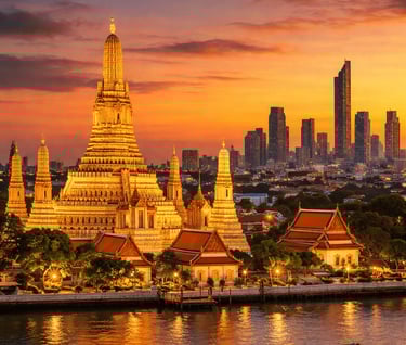 Wat Arun in Bangkok bei Sonnenuntergang mit dem Chao-Phraya-Fluss und der Skyline der Stadt.