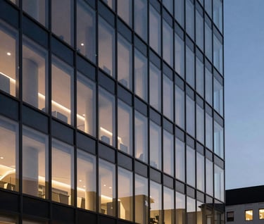 A cinematic architectural photograph of a sleek, modern North American building facade at twilight. The glass reflects a muted indigo sky, with internal warm ivory lights creating a professional and restrained geometric pattern.