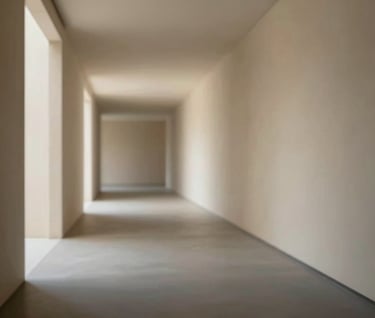 An ethereal shot of a minimalist corridor where light spills from an unseen courtyard, washing over charcoal-colored floors and sand-colored walls. Professional architectural photography.
