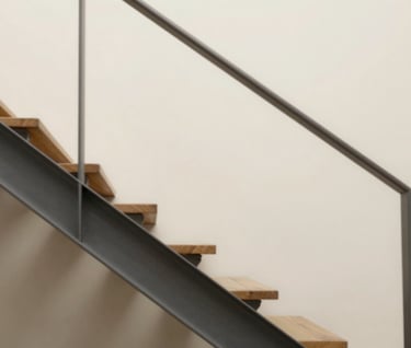 Clean architectural detail showing a staircase made of wood and metal, casting geometric shadows on a sand-colored wall (#F9F7F2). Soft, diffused natural light.