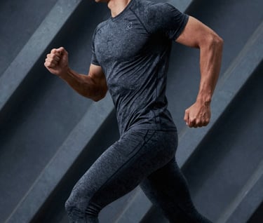 A dynamic shot of a male model in motion, wearing dark graphite activewear, set against an industrial AI-generated background of geometric metal structures and cool blueish-grey shadows.