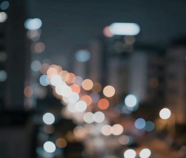 Abstract cinematic shot of blurred city lights at night, creating a soft bokeh effect in shades of #4A616F and #8C9CA6 against a dark #1A1A1A background, conveying a sense of modern motion.