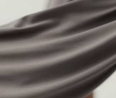 Abstract detail shot showing movement and motion blur of fabric. The colors are muted #4A616F and #1A1A1A, suggesting a high-speed cinematic capture with professional lighting.