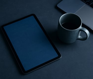 A top-down flat lay of a minimalist workspace in a South American / Brazilian home office. A high-end tablet displays a book cover, positioned next to a ceramic cup. The palette is dominated by dark blue and steel blue.
