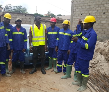 A group of African construction workers wearing blue overalls and hard hats at a building site.