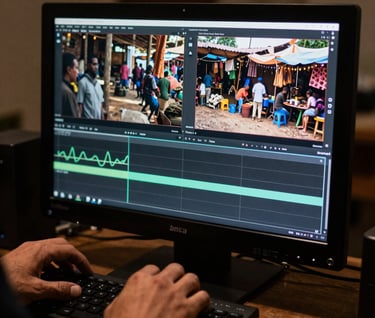 Detail of a filmmaker's hands editing a video on a professional monitor, showing a scene of an Angolana market, cinematic dark room environment.