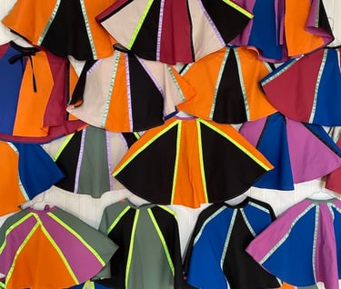Collection of colorful handmade capes in vibrant block patterns and neon stripes for kids costumes.