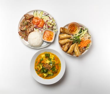 a variety of food items on a table including curry, rice with char siu, and spring roll salad.