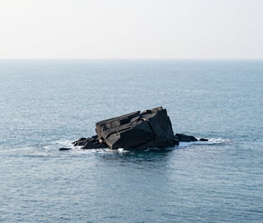 A wide minimalist coastal landscape, featuring a single dark rock formation emerging from a pale ice blue ocean, soft natural lighting, serene atmosphere, high-resolution photography, International / Western.