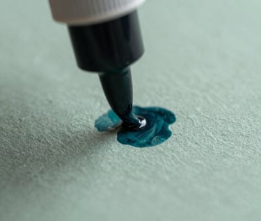 Macro shot of ink being applied to a textured, eco-friendly paper surface during the printing process. Artistic and sophisticated, emphasizing craft and editorial excellence. Muted teal and sage color palette.