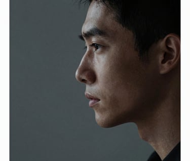 A detailed portrait photograph of a character's profile, illuminated by a pale mist light source from the side. The background is a clean dark slate grey. The composition is artistic with a shallow depth of field, set in a North American / US environment.