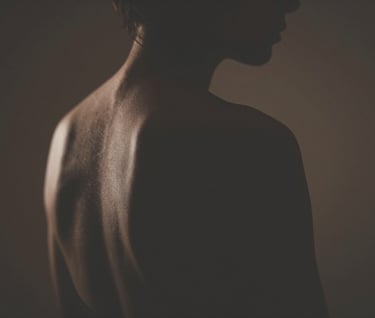 A silhouette of a human form against a dimly lit background, emphasizing the curvature of the back and shoulder, soft edges, deep shadows, warm lighting using #4C4A48 and #F5F2EF.