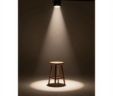 Artistic shot of a photography studio setup. A single stool under a dramatic spotlight #F5F2EF in a dark room #1F1E1C. Represents the preparation for a lifestyle shooting d'art. Sophisticated, warm, and inviting mood.