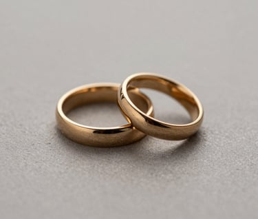 A minimalist macro photograph of two metallic gold wedding rings placed on a textured neutral medium gray surface. The lighting is soft and focused, creating a premium feel.