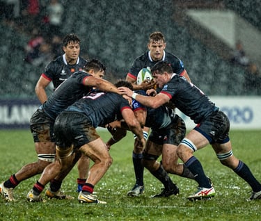 Intense wide shot of a rugby match in the rain. Players in dark jerseys clashing in a scrum, water droplets and mud splashing, sharp cinematic lighting, professional sports photography, Western / International.