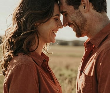 An intimate portrait of a couple laughing, foreheads touching, in a sun-lit field. North American US fashion. The mood is authentic and deeply emotional with warm terracotta tones.
