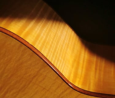 Close-up of a hollow body acoustic guitar with a natural flamed maple wood finish and dark binding.