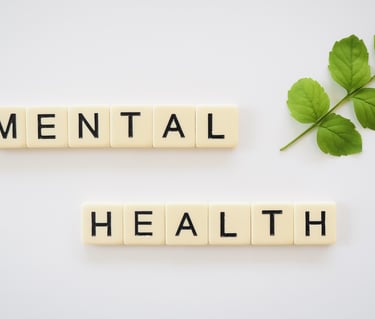 Mental health text spelled with letter tiles next to a green leaf on a white background.