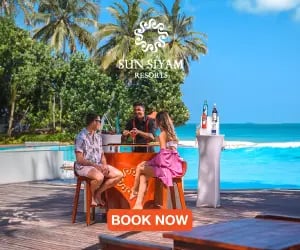 A couple enjoys cocktails at a tropical Sun Siyam beach resort bar overlooking the ocean.