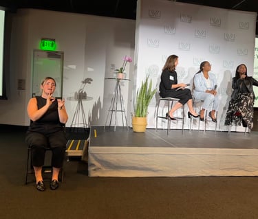 a stage with three business professionals, and a sign language interpreter to the side