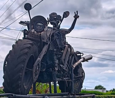 Custom-built post-apocalyptic steampunk motorcycle sculpture with large tractor tires and metal scrap parts.
