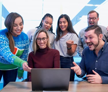Diverse business team celebrating success while looking at a laptop screen in a bright office.