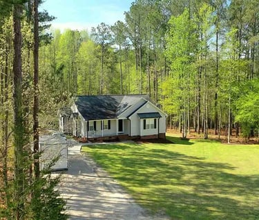Scenic aerial view of a house with a lawn and gravel driveway surrounded by tall pine trees.